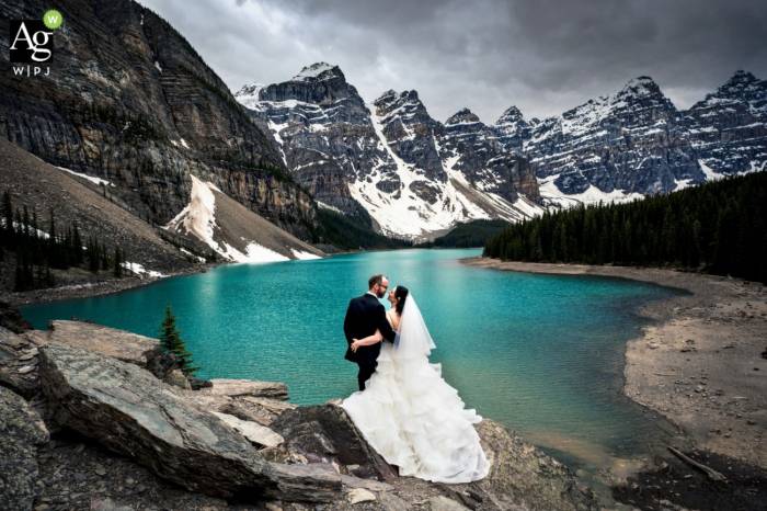 Bride and Groom at Moraine Lake looking at each other. In front of them amazing Mountain View and a blue lake. Best Banff Wedding Photography.
