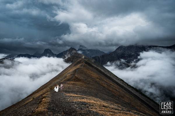 Fearless couple at the top of the mountain walking at the ridge in Banff. On the background stunning Rocky Mountains and heavy clouds.