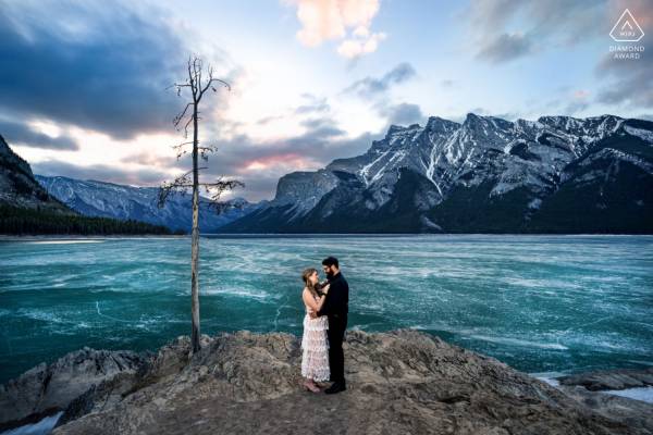 Winning Engagement Photograph from Banff. Couple standing by the frozen Minnewanka Lake in a hug.