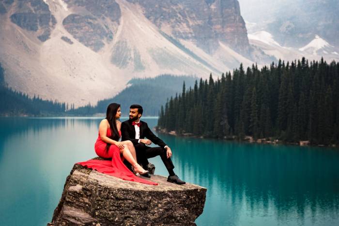 Engaged people sitting at the giant rock and look at each other during Moraine Lake engagement photo session with 4Eyes Photography Canada.