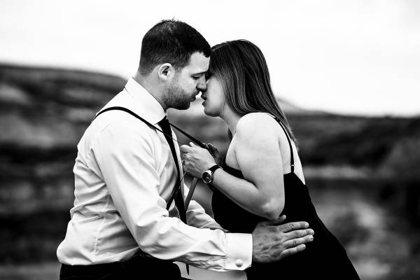 Lady pulls his fiancees harness and kisses him. Black and white engagement photography captured by Calgary Wedding Photographer Eliza Slobodzian