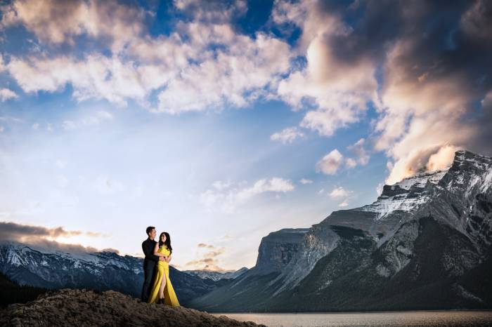 A man hugging his fiancee in a yellow dress in the stunning location of Minnewanka Lake in Banff during amazing sunrise.