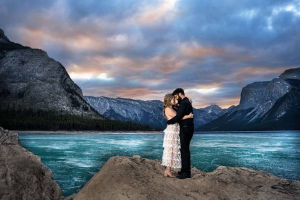 Couple in love in a hug at frozen Minnewanka Lake during stunning and colorful sunrise.