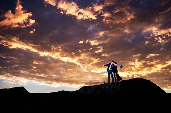 Engaged couple standing up the hill and kissing during colourful sunrise in Calgary. Amazing Engagement and Wedding Photography captured by Lukas SlobodzianL