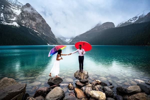 Newly engaged couple stand on the rocks in the rain during Lake Louise Engagement Session