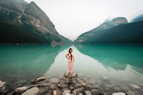 Gorgeous Indian lady standing on the rock at Lake Louise. She has long black hair and wearing long pink dress.