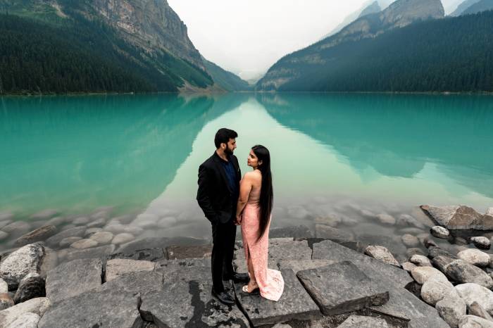 Handsome Indian couple look at each other at Lake Louise during their engagement photo session.