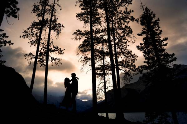 Engaged couple look at each other at Minnewanka Lake during the sunrise