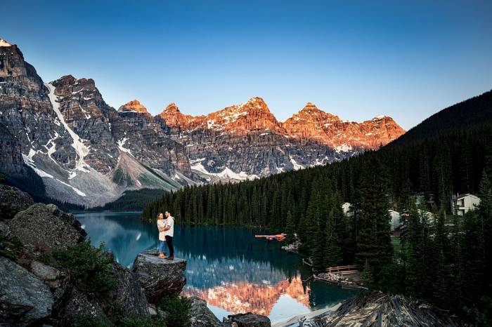 Engaged couple standing at the rock at Moraine Lake. On the background tremendous mountains and blue lake.