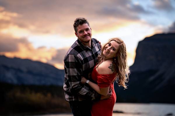 Couple in love are smiling and looking at the camera. They are posing to Banff Wedding Photographer during engagement photo session at Minnewanka Lake.