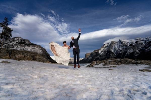 newlyweds jump at frozen Minnewanka Lake . The moment captured by Calgary Wedding Photographer.