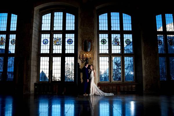 Bride and groom; s portrait in the Fairmont Banff Springs hotel. They lean against the wall nest to the huge windows with the Rocky Mountains. view.