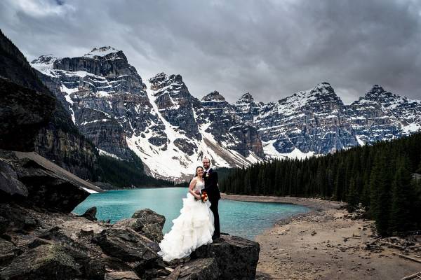 Bride's and Broom's portrait at Morainne Lake. They stand on the rock against stunning mountain view and blue lake.