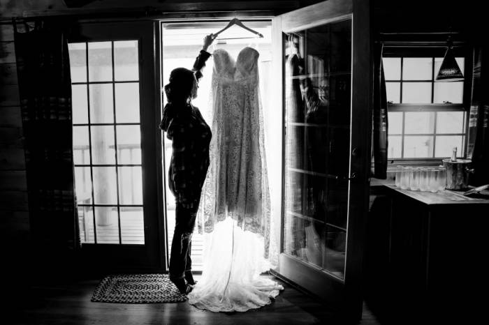 Bride reaches for her wedding dress which hangs on the window.