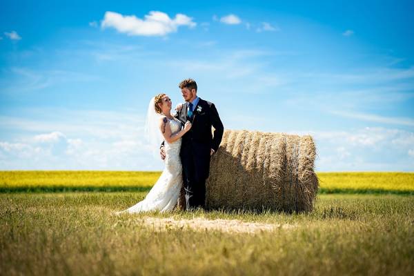 Bride and groom lean over a hay barrel during after-wedding session in Calgary. They look at each other and smile.