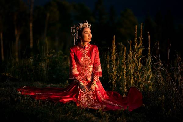 Traditional Korean bride's portrait. The bride wears stunning Korean , red wedding dress and sits on the grass.