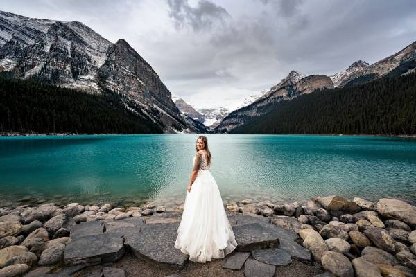 Bride in a white wedding dress adore the beauty of Lake Louise in Banff National Park. She glanced at her Calgary Wedding Photographer and gave a smile.