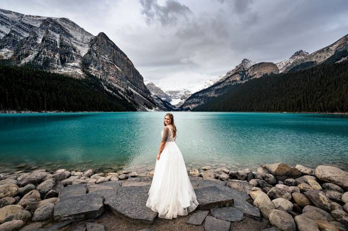 Bride in a white wedding dress adore the beauty of Lake Louise in Banff National Park. She glanced at her Calgary Wedding Photographer and gave a smile.