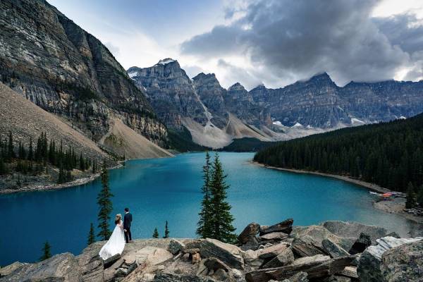 Bride and Groom adore tremendous mountains and blue Moraine Lake in Banff National Park.