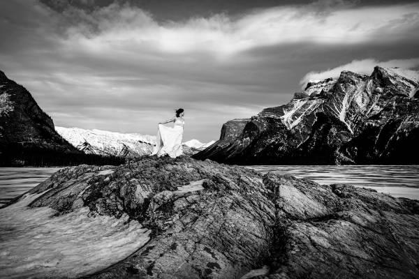 Bride's portrait in black and white. She stands at the giant rock at frozen Minnewanka Lake in Banff.