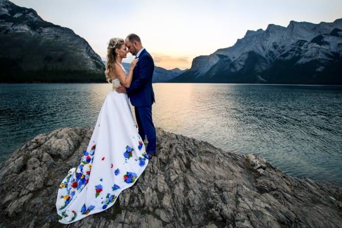 Bride and groom facing teach other and touching their foreheads. They are at Minnewanka Lake posing to Banff Wedding photographer during sunrise.