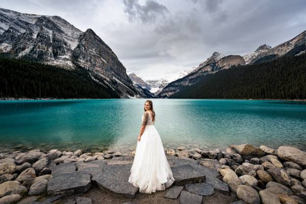 Stunning bridal portrait at Lake Louise. taken by Banff Wedding Photographers. The bride is standing by the Lake Louise and look at the Banff Wedding Photographer.