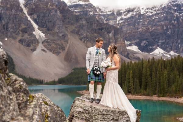 Newlyweds look at each other surrounded by Rocky Mountains at Moraine Lake in Banff.