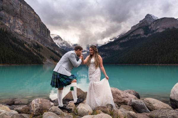 Groom kissing the bride's hand during elopement ceremony at Lake Louise.