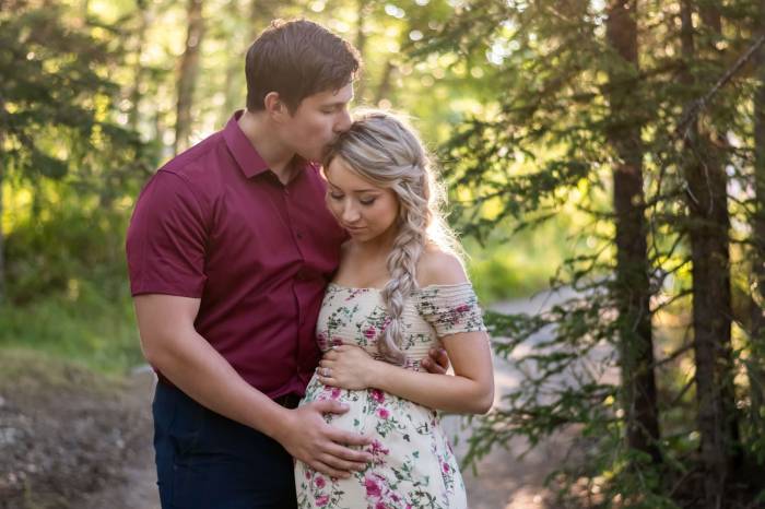 Maternity photo session in Banff. A man touches his pregnant wife's belly and kisses her forehead.