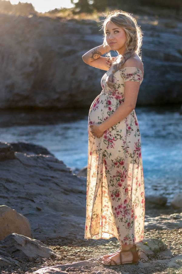 Maternity portrait in Banff. Pregnant woman touches her bally and smiles at the camera.