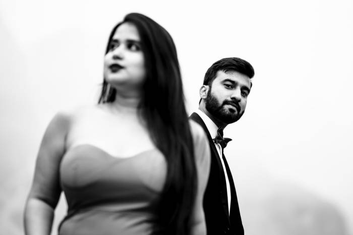 Man is looking at the camera and his fiancee is looking away. Black and white photography.