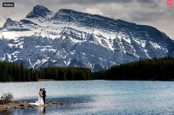 Wedding Award Photo of newlyweds standing by the edge of the lake in Banff. They ate surrounded by amazing Canadian Rockies.