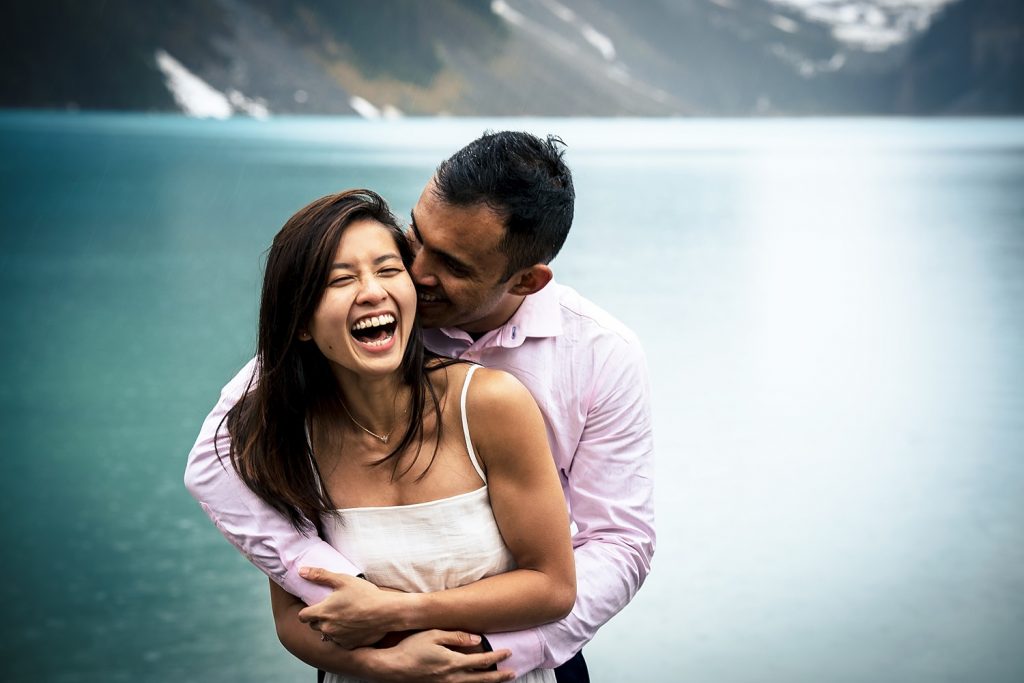 Happy moment during engagement session at Lake Louise. Man whispers to the girl's ear and she laughs. | 4Eyes Photography