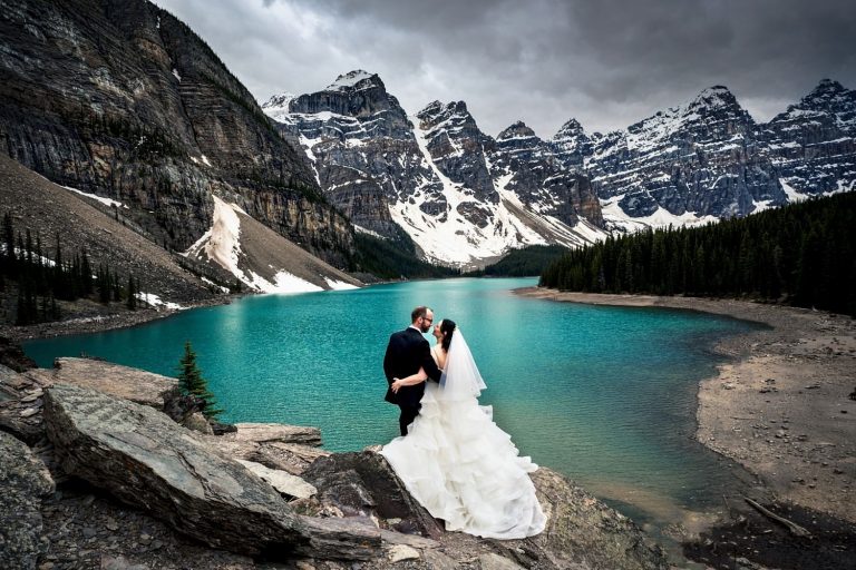 Wedding portrait at majestic Moraine Lake in Banff. Couple admire the beauty of the lake and mountains.