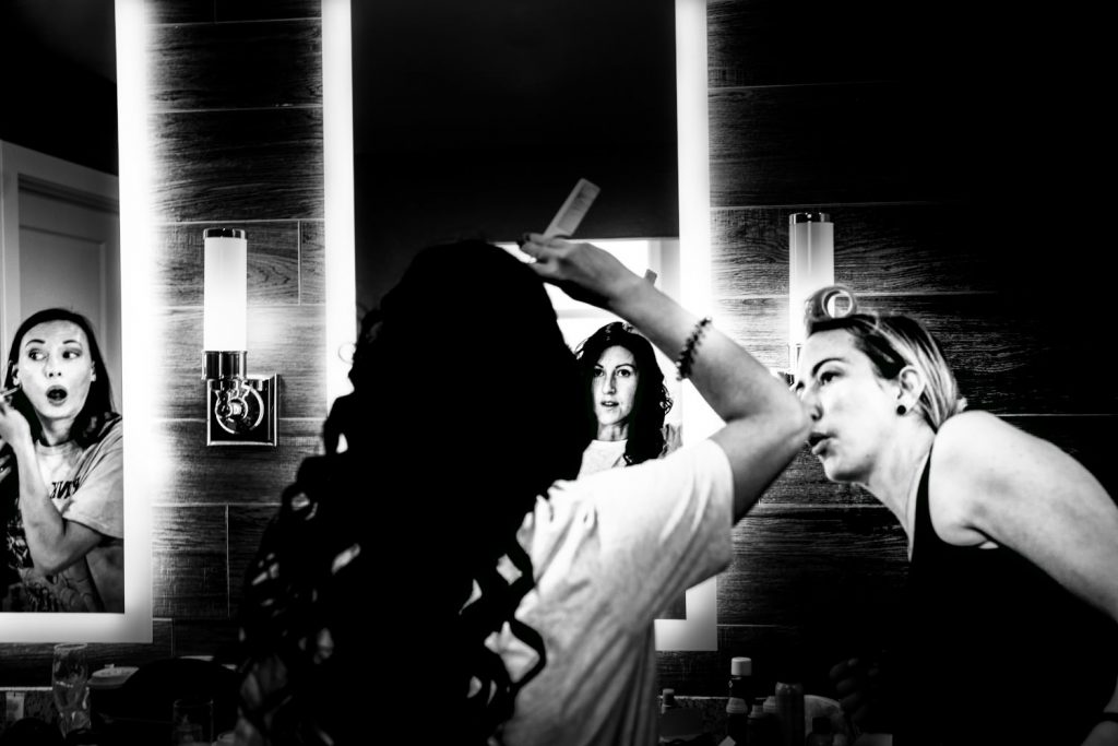 Bride fixing hair hair in the mirror while her friend look at her. | 4Eyes Photography