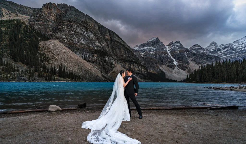 Bride and groom stand at the lakeshore at Moraine Lake