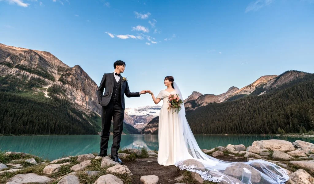 Bride and groom hold hands at lake Louise