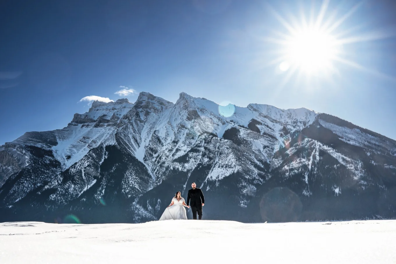 Newlyweds walk at the frozen lake in Banff. Behind them tremendous mountain covered with snow.