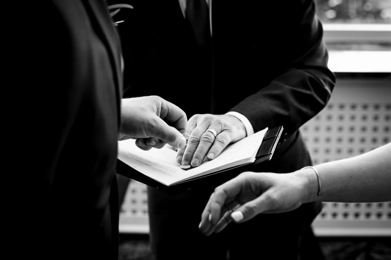 Groom reaches to get the wedding ring from the officiant's book. Banff Wedding Photographer captured the moment of moving hands and the ring.