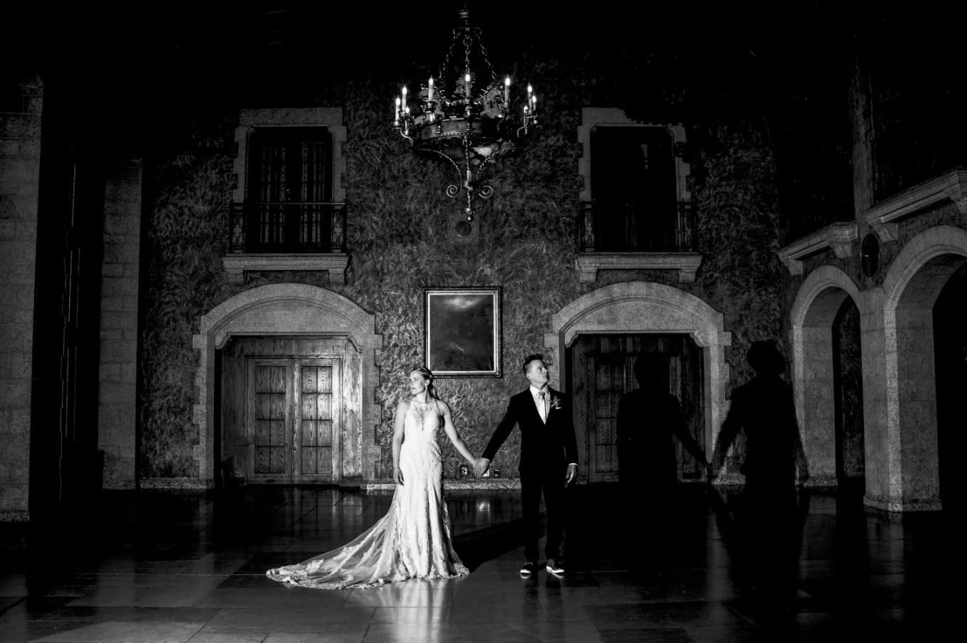 Newlyweds portrait session taken by Banff Wedding Photographer in the ball room at Fairmont Hotel. They fold their hands, above them stunning chandelier.