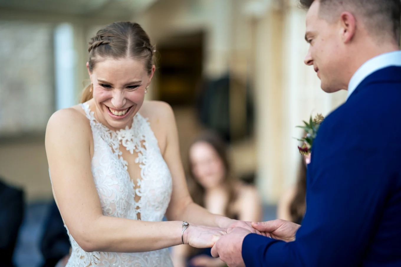 Bride and groom hold their hands while the bride laughs during groom's speech.