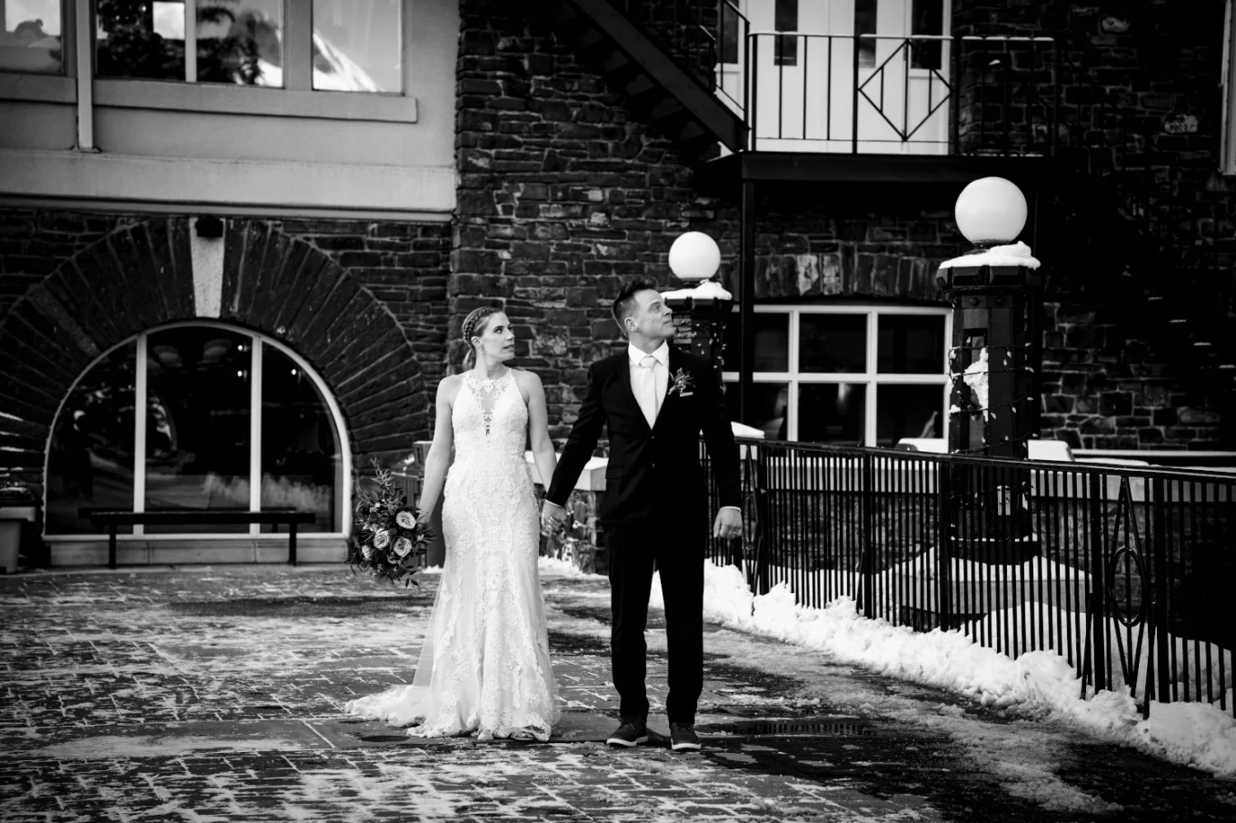 Newlyweds walk holding their hands in front of the Fairmont Hotel Springs in Banff.