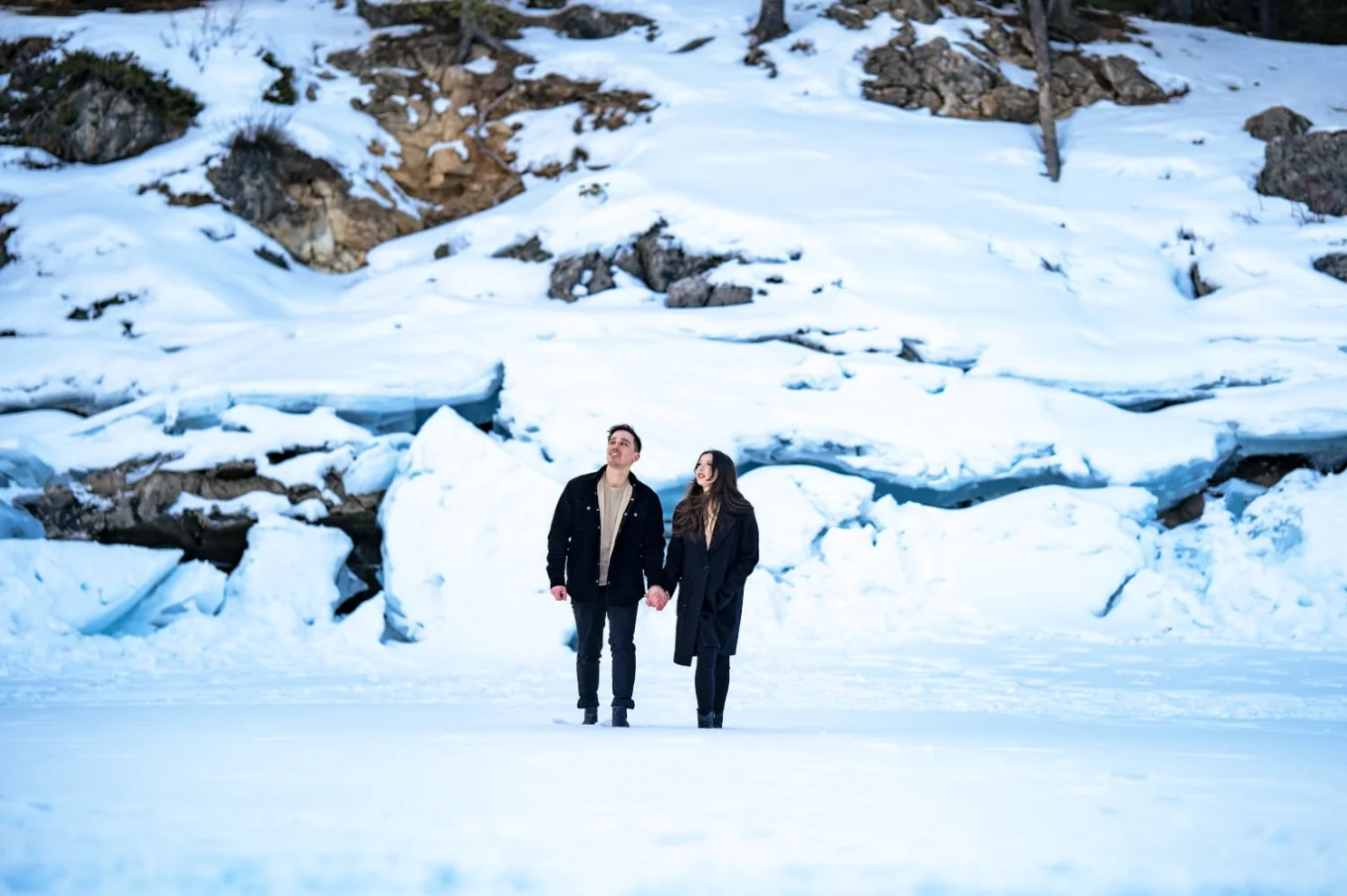 Couple lovers in black walking at the frozen lake behind them a wall of frozen snow.