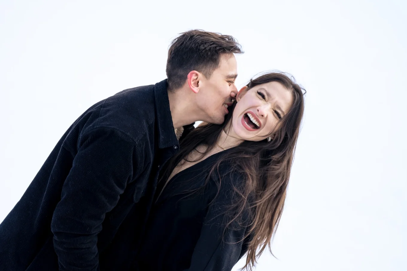 A man kisses his fiancee on her neck while she laughs. Fun engagement photo-shoot with amazing Calgary Wedding Photographer.