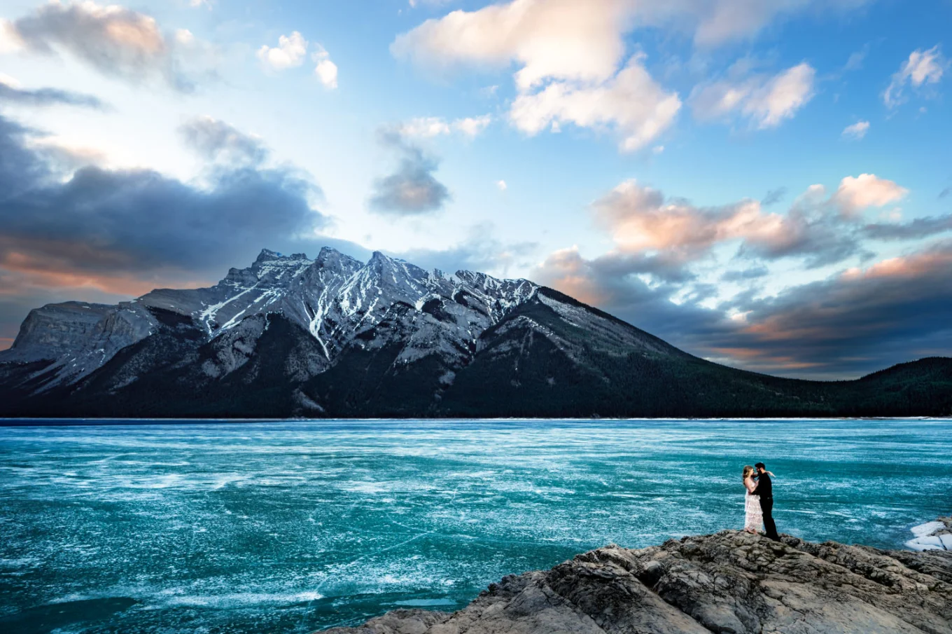 Tiny people standing at the rock at the frozen Minnewanka Lake in the mountains.