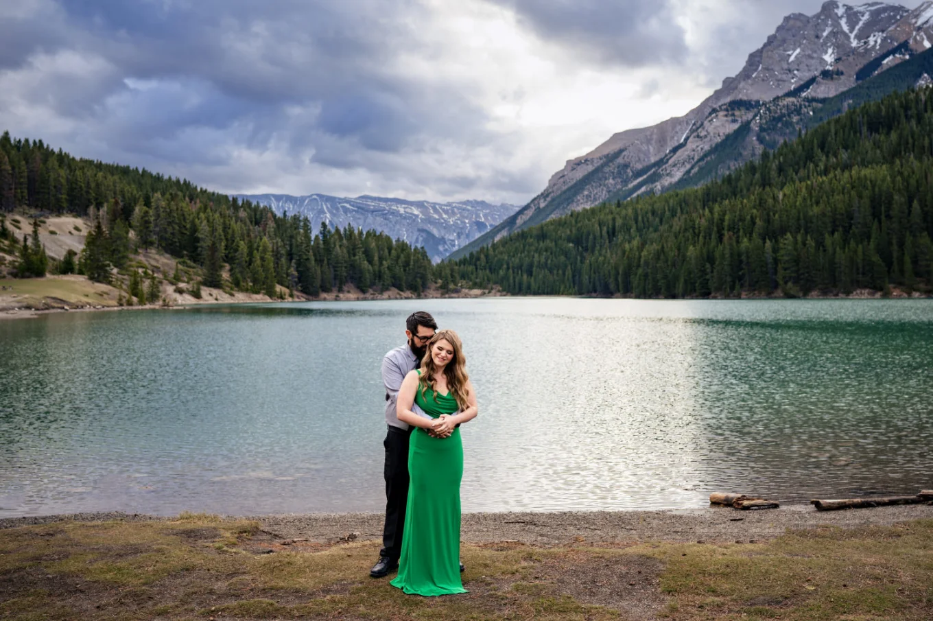 Romantic photograph of the man hugging his fiancee in a green dress. Photograph at Two Jack Lake in Banff.