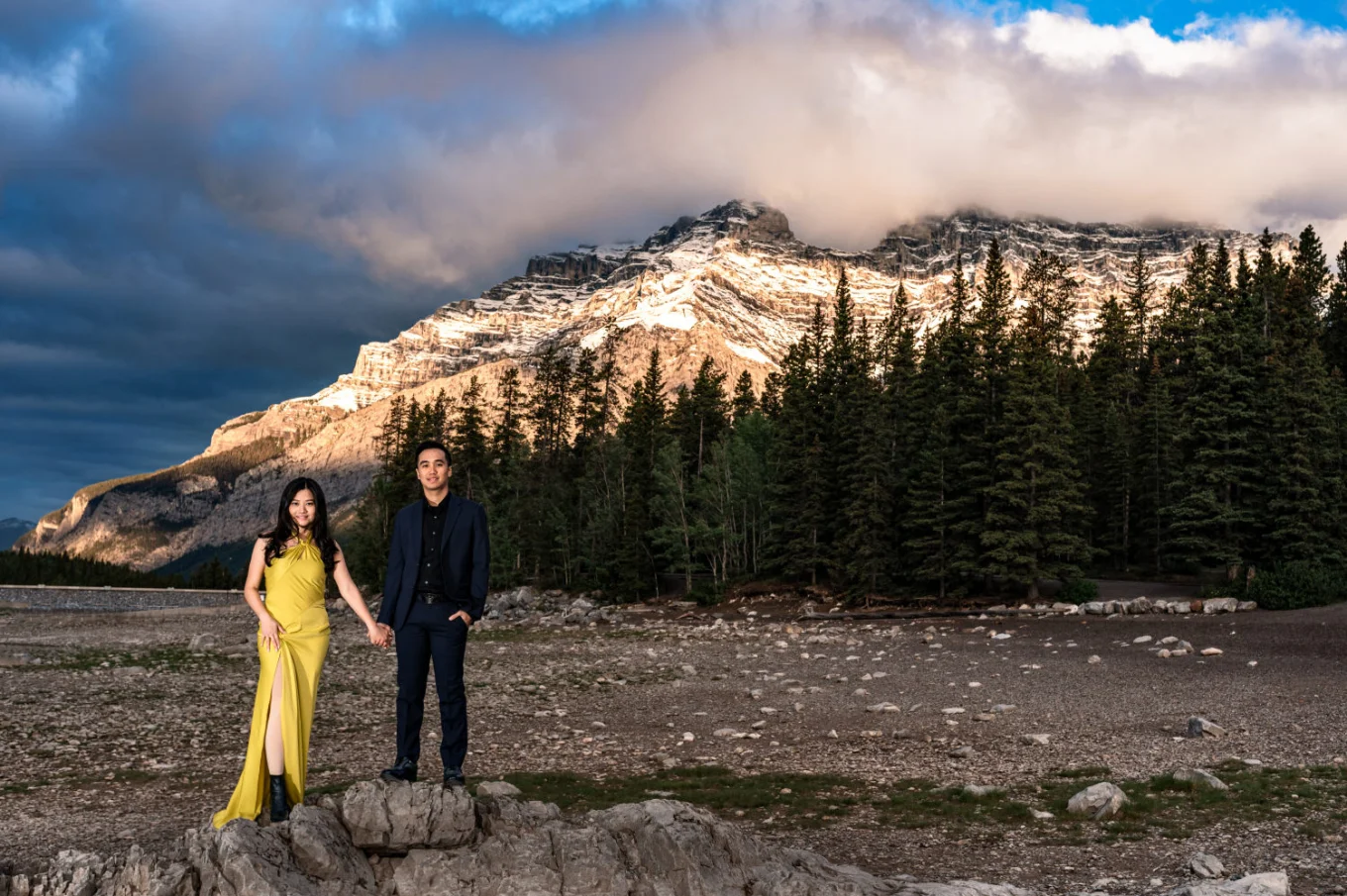 Lady in a yellow dress and her fiancee stand at the rock in Banff during an engagement session performed by the best Banff Wedding Photographer.