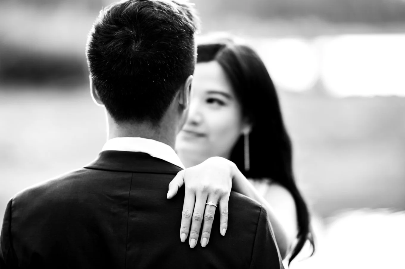 Photograph in Black and white of the couple looking at each other. Her hand on his arm with the big engagement ring.