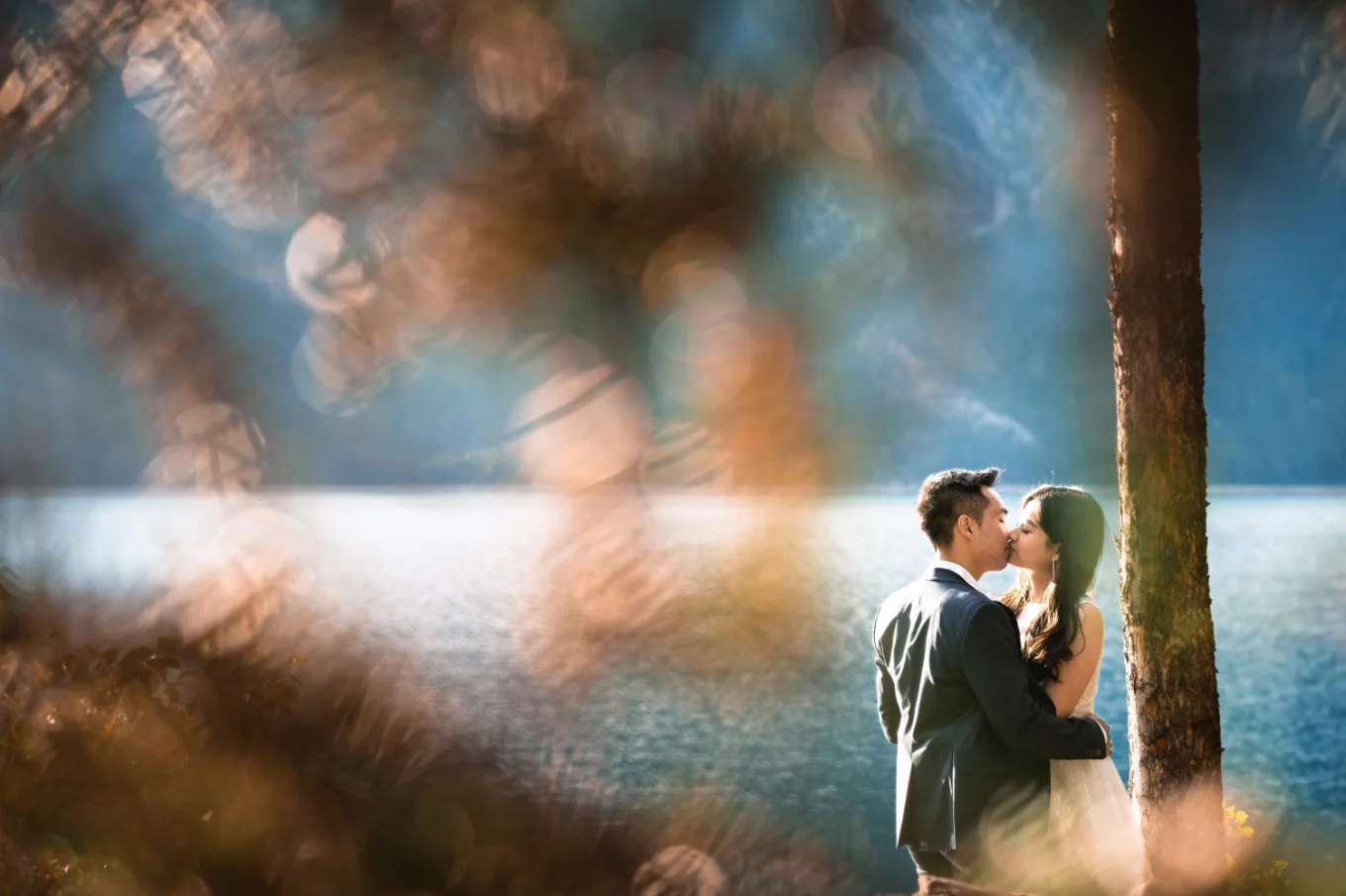 Engaged couple share a kiss by the Minnewanka Lake . Photo taken by Banff Wedding Photographers.