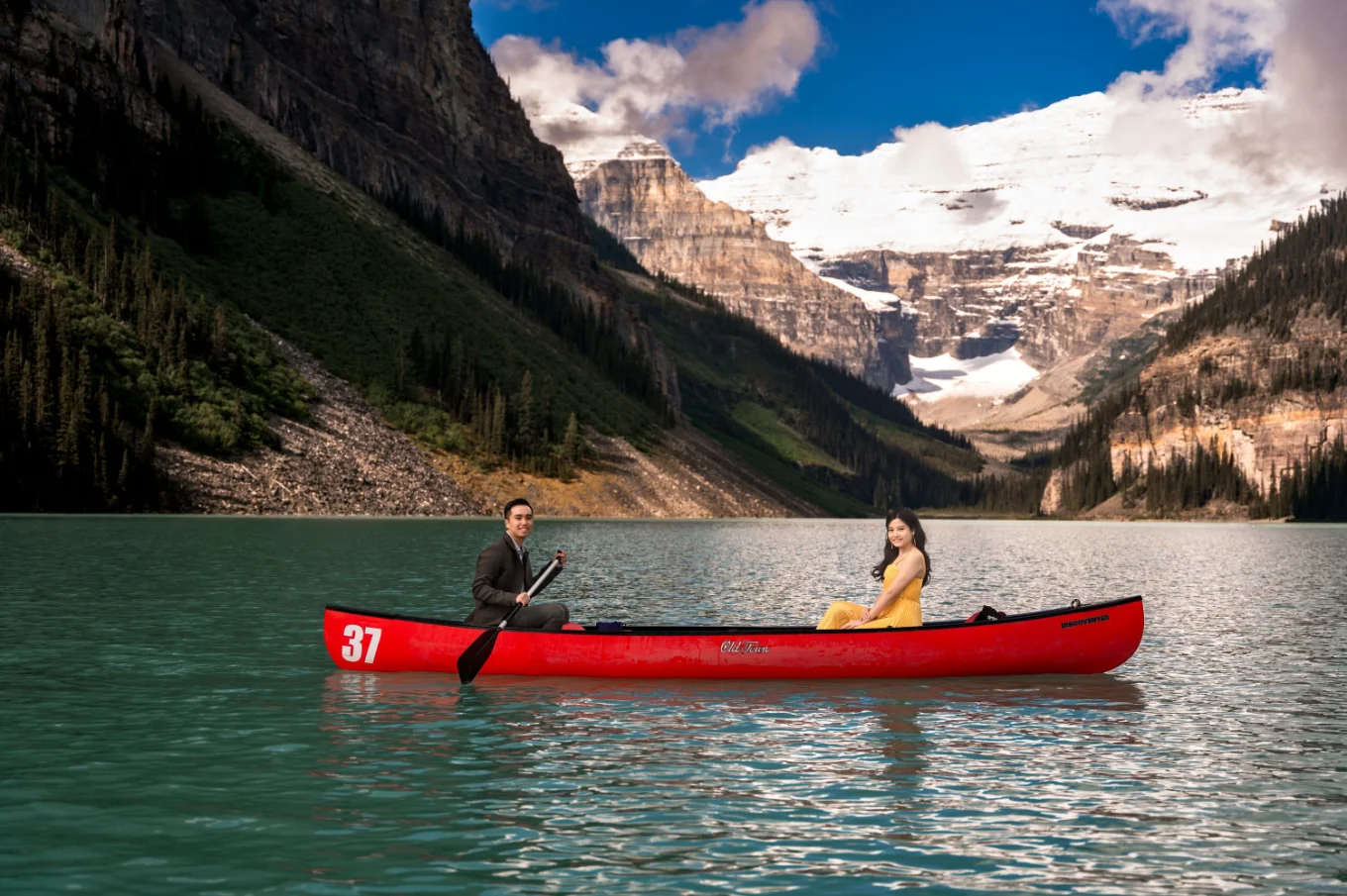 Lady in a yellow dress and a gentleman in a suite paddling in the red canoe at Lake Louise.